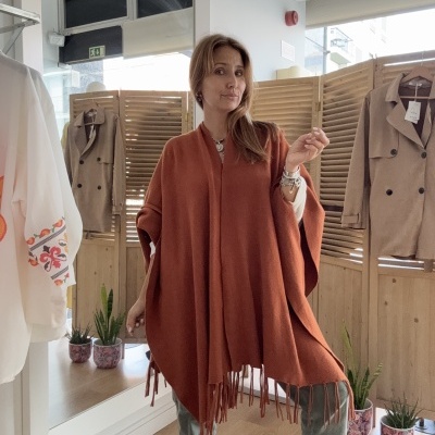 Poncho castanho com franjas usado numa loja com divisórias de madeira e plantas