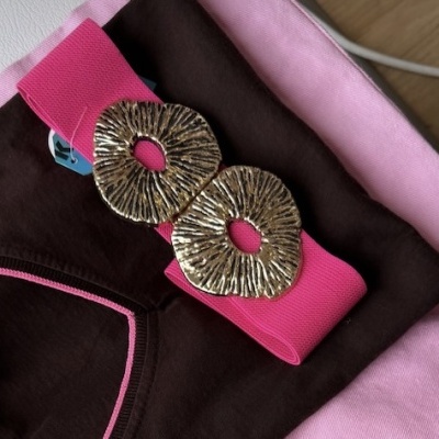 Cinto rosa com fivela dourada sobre roupa castanha e tecido rosa