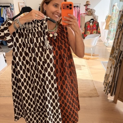 Vestido feminino castanho com bolinhas pretas em tecido leve segurado numa loja de roupas.
