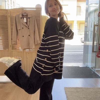 Mulher a usar malha riscada preta e branca em loja com casaco pendurado