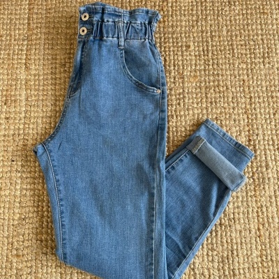 Calças de ganga azuis com cintura elástica e botões numa superfície de tapete de fibras naturais