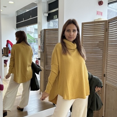 Mulher vestindo camisola amarela de malha e calças brancas com fundo de loja