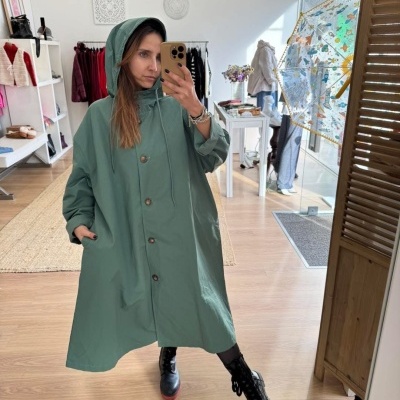 Capa impermeável verde com capuz e botões, mulher a tirar selfie numa loja