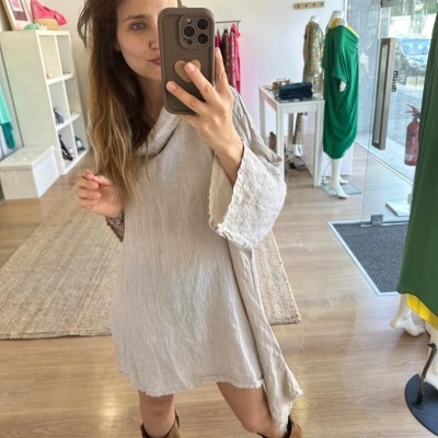Mulher tira selfie com vestido bege de manga comprida e botas castanhas em loja com manequins ao fundo