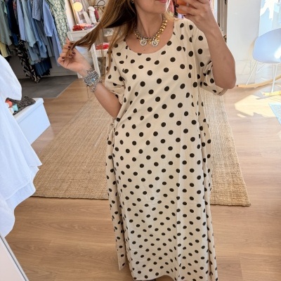 Mulher a usar vestido comprido bege com bolinhas pretas na loja
