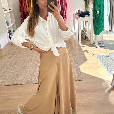 Mulher com camisa branca e saia bege numa loja de roupa, roupa pendurada e manequim verde ao fundo