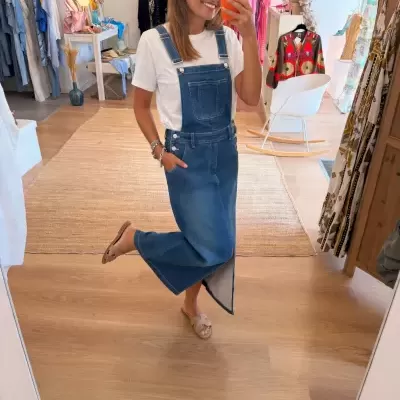 Pessoa com vestido jardineira de ganga azul e camiseta branca numa loja de roupa