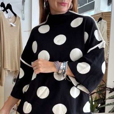 Camisola preta de malha com bolinhas brancas usada por mulher em interior.