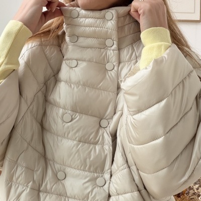 Casaco acolchoado bege claro com botões, gola alta em ambiente interior.