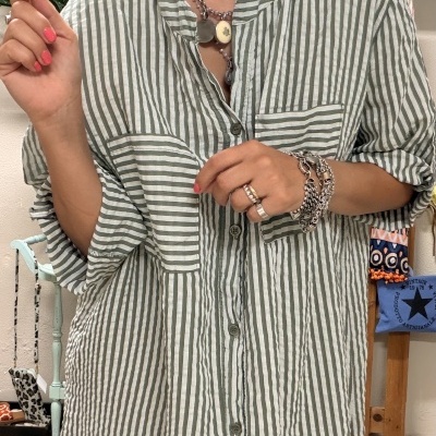 Camisa longa riscada cinza e branca com botões e bolso, mulher com acessórios prata e decoração ao fundo