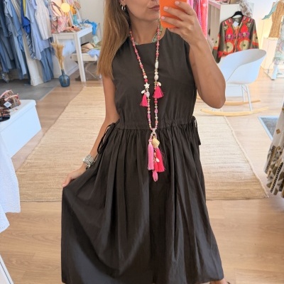 Mulher com vestido preto longo e colar rosa a tirar selfie numa loja de roupa.