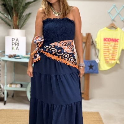 Mulher com vestido azul escuro e lenço colorido à volta da cintura em ambiente interior decorado