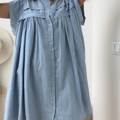 Vestido azul claro com botões e mangas curtas usado por pessoa com óculos grandes em ambiente interior.