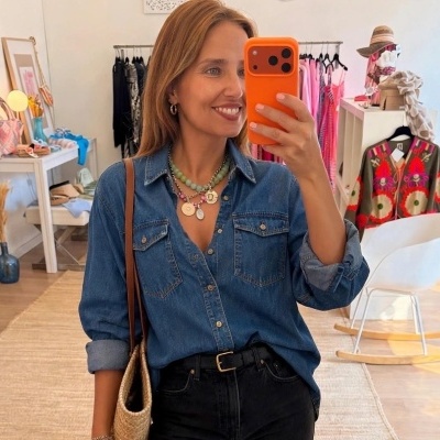 Mulher com camisola azul de ganga e colar colorido a tirar selfie num espelho em loja de roupa