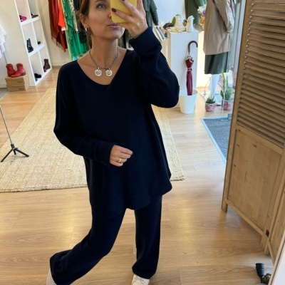 Mulher de roupa preta e sapatilhas brancas a tirar selfie em loja de roupa com chão de madeira e cabides ao fundo