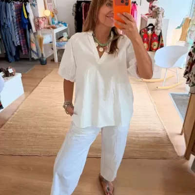 Conjunto branco feminino com blusa de mangas bufantes e calças, selfie num espaço de roupa