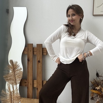 Mulher com camisola branca e calças largas castanhas em ambiente interior minimalista