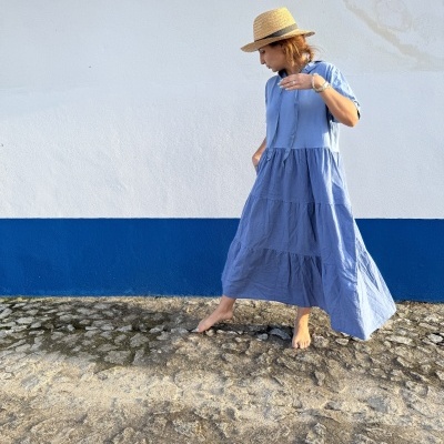 Mulher a usar vestido azul claro e chapéu de palha junto a parede branca e azul.