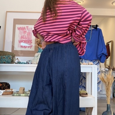 Mulher de costas com camisola rosa de riscas e calças largas azuis em loja