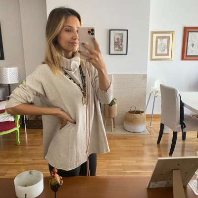 Mulher com camisola bege a tirar selfie num espelho numa sala com chão em madeira e decoração variada