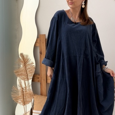 Mulher com vestido azul escuro e botas pretas em ambiente interior com espelho ondulado