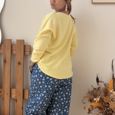 Pessoa de costas com camisola amarela e calças azuis com bolinhas brancas num ambiente interior decorado.