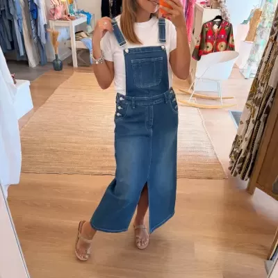 Vestido macacão de ganga azul médio com bolso frontal e alças reguláveis num provador com roupas ao fundo