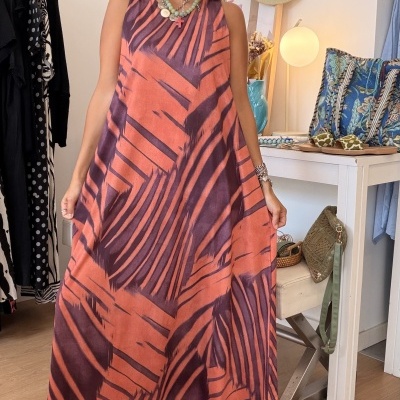 Vestido comprido laranja e roxo com padrão abstrato e sandálias castanhas em ambiente de loja