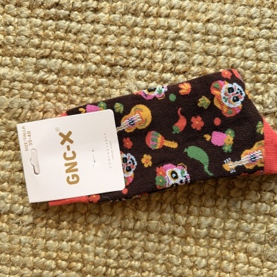 Meias GNXC castanhas com padrão colorido de caveiras e pimentos numa etiqueta branca sobre tapete claro