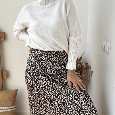 Saia comprida animal print e camisola branca de gola alta em ambiente interior