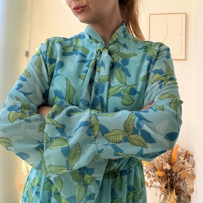 Vestido azul claro com padrão de folhas verdes e azuis e gola alta com laço.