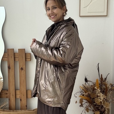 Mulher com casaco bronze brilhante e vestido castanho num ambiente interior decorado.