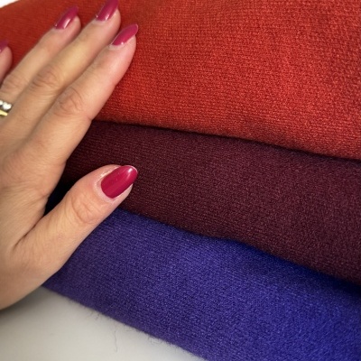 Três tecidos de malha em laranja, bordô e roxo com mão tocando o tecido laranja