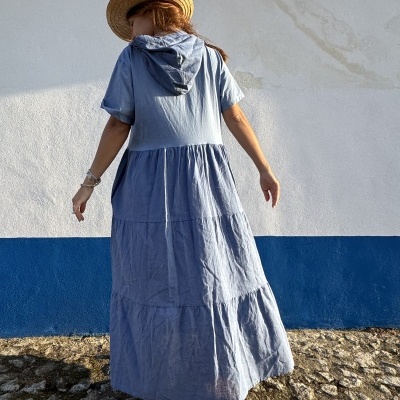 Vestido longo azul claro com capuz usado por pessoa de chapéu de palha, vista de costas