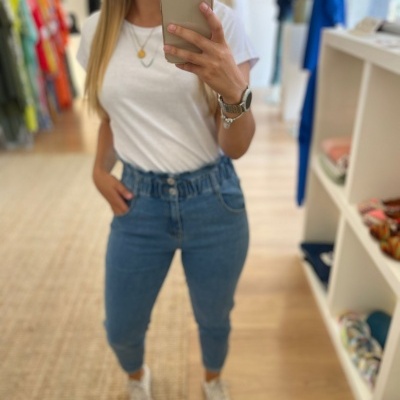 Mulher com t-shirt branca, jeans azuis de cintura alta e sapatos brancos, a tirar selfie num espelho