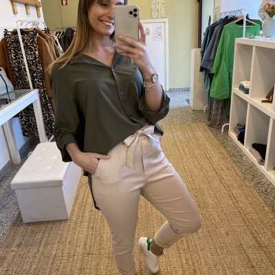 Mulher com calças bege e camisa verde-tira selfie em espelho numa loja