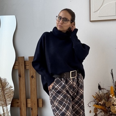 Mulher com óculos, camisola azul escuro, calças xadrez e botas pretas em ambiente rústico