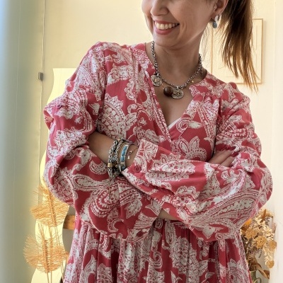 Vestido vermelho com padrão branco, colar e pulseiras metálicas em ambiente interior