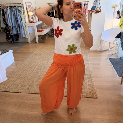 Camiseta branca com flores coloridas e calças largas laranja.