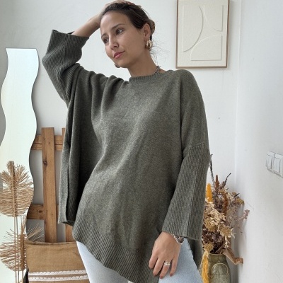 Mulher com camisola verde musgo e calças claras em ambiente decorado