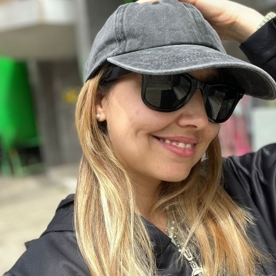 Mulher com boné cinzento e óculos de sol pretos, casaco preto, cabelo loiro