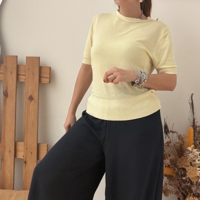 Mulher com blusa amarela e calças pretas em ambiente interior decorado