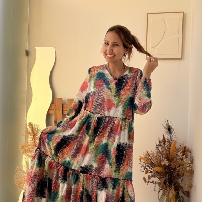 Mulher a usar vestido comprido colorido com padrão abstrato em fundo claro com decoração