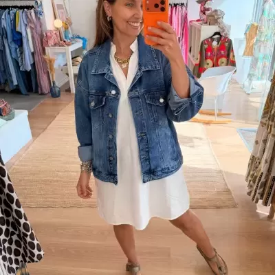 Mulher com casaco de ganga azul e vestido branco numa loja de roupa colorida