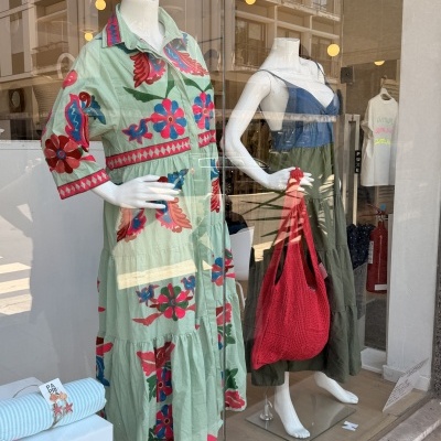 Mannequin com vestido verde floral e outro vestido verde e azul com bolsa vermelha na vitrine