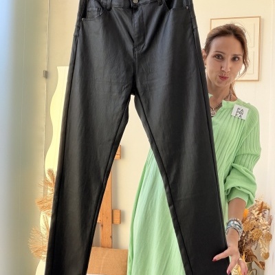 Calças pretas estilo pele seguradas por mulher com vestido verde