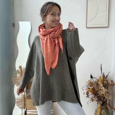 Mulher com camisola cinza, cachecol rosa, jeans claros e botas Hunter, em ambiente interior com espelho e flores secas