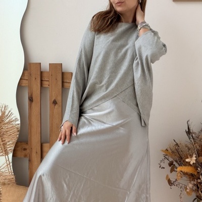 Mulher com blusa cinza, saia prateada e botas pretas em ambiente interno minimalista