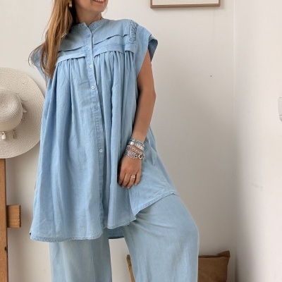 Mulher com conjunto azul claro de blusa e calças largas em ambiente interior