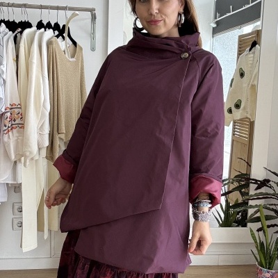 Mulher com casaco roxo e saia floral em ambiente interno com cabideiro e espelho